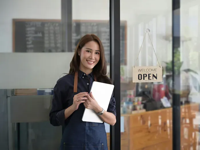 Smiling small business owner standing by the “Open” sign in her shop, representing friendly local services on townserviceindex.com